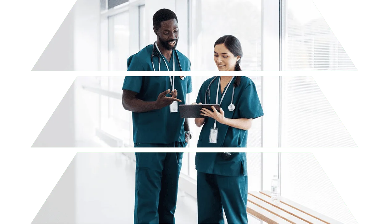 A healthcare worker in scrubs uses a tablet, engaged in a task, in a medical environment.