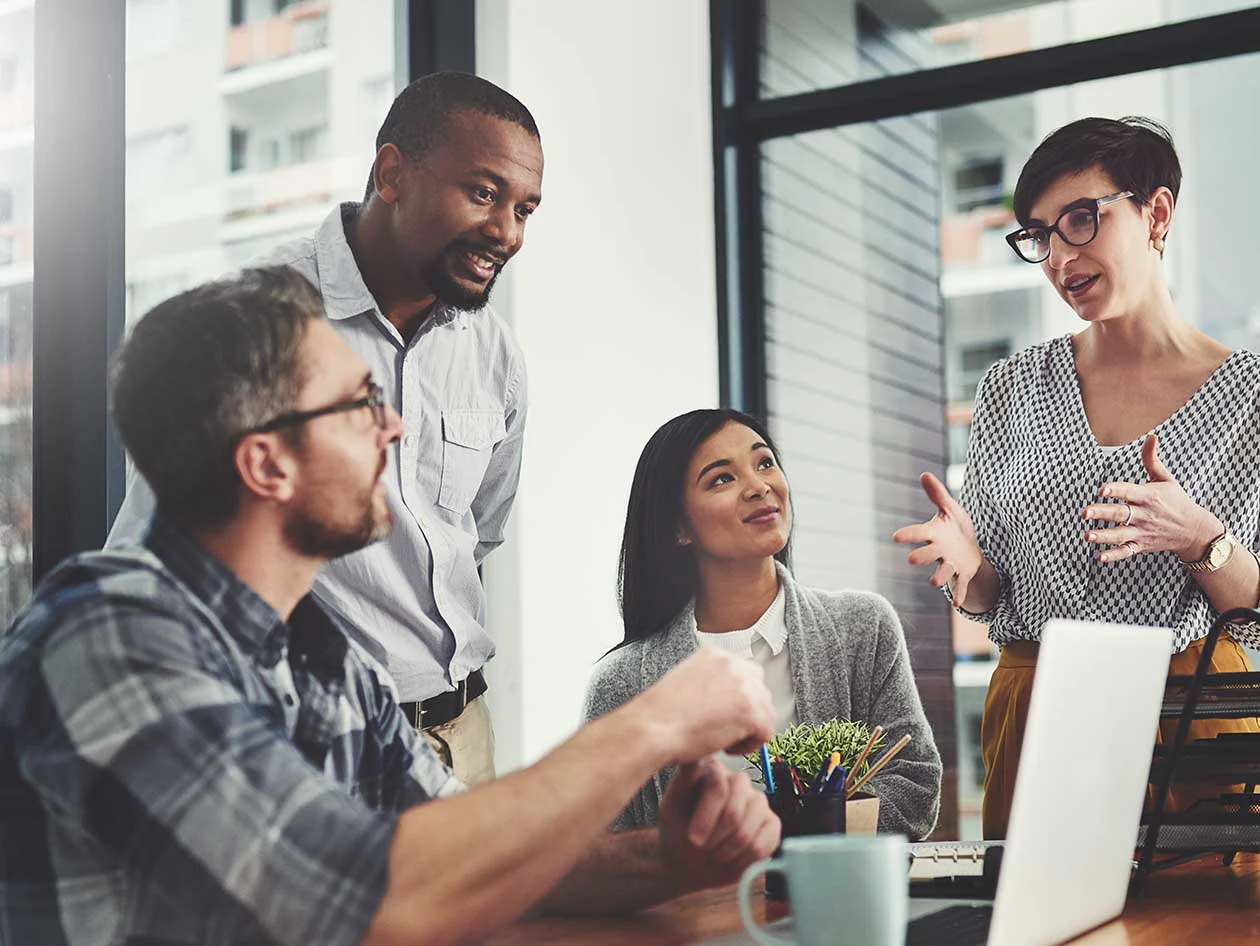 A group of business people gathered around a laptop in their office